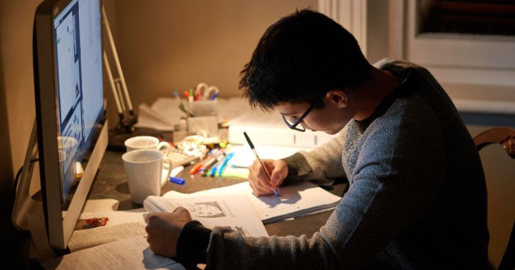 Student studying at a desk with textbooks, notes and a computer.